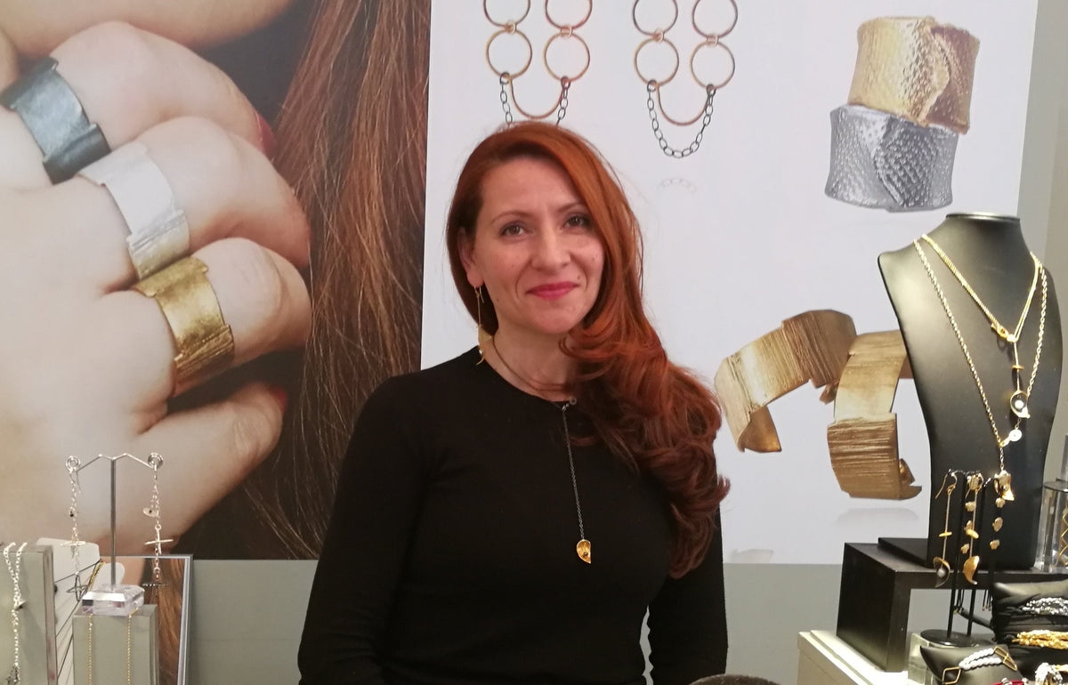 Athenart founder and Greek jewelry designer Athena Papa at an exhibition surrounded by her handmade jewelry designs.