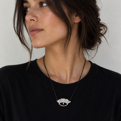 Woman wearing a black top and a necklace with a decorative pendant against a neutral background
