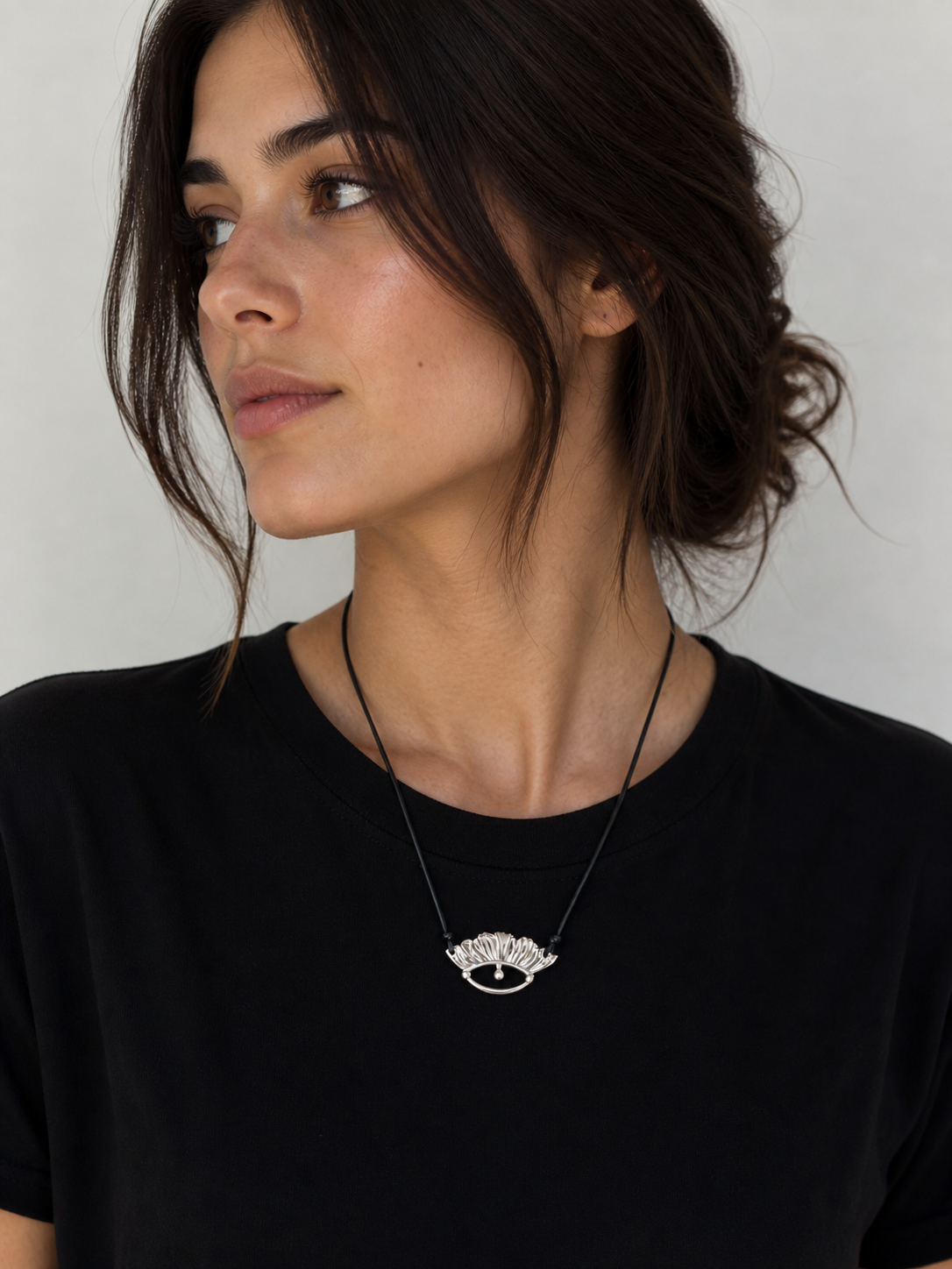 Woman wearing a black top and a necklace with a decorative pendant against a neutral background