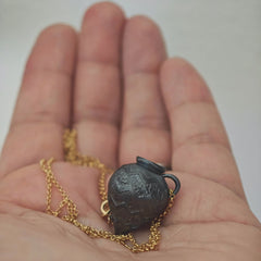 Close-up of the Ancient Whisper Amphora pendant resting on a hand