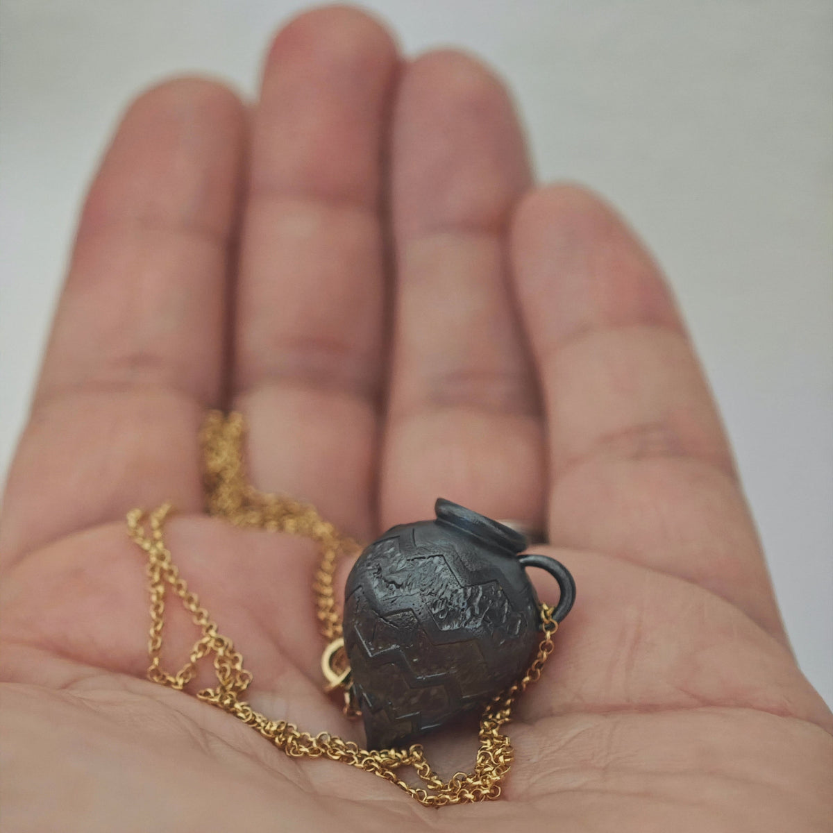 Close-up of the Ancient Whisper Amphora pendant resting on a hand
