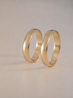 Two polished yellow gold wedding bands standing upright on a neutral beige background.