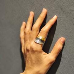 Hand wearing a silver and gold ring on a gray background