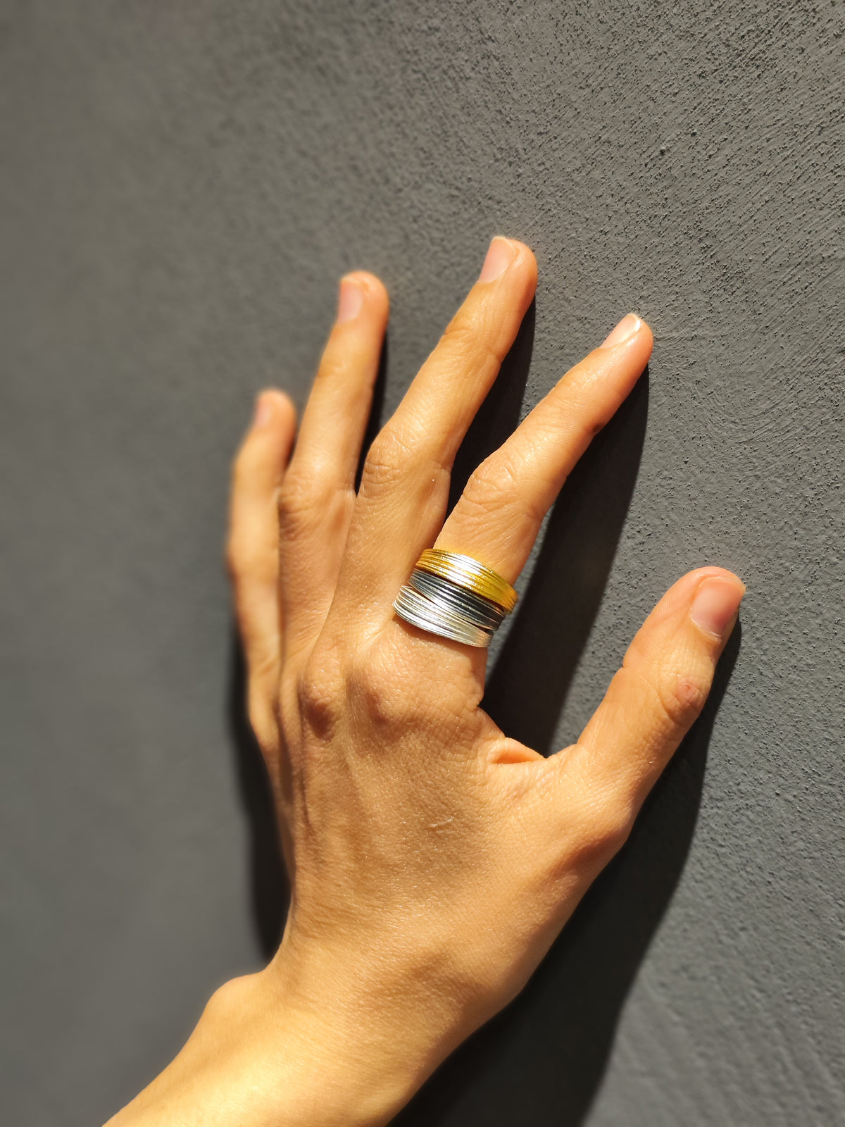 Hand wearing a silver and gold ring on a gray background