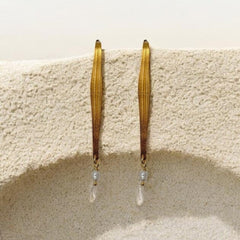 Gold hoop earrings with pearl-like beads hanging on a textured beige surface.