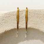 Gold hoop earrings with pearl-like beads hanging on a textured beige surface.