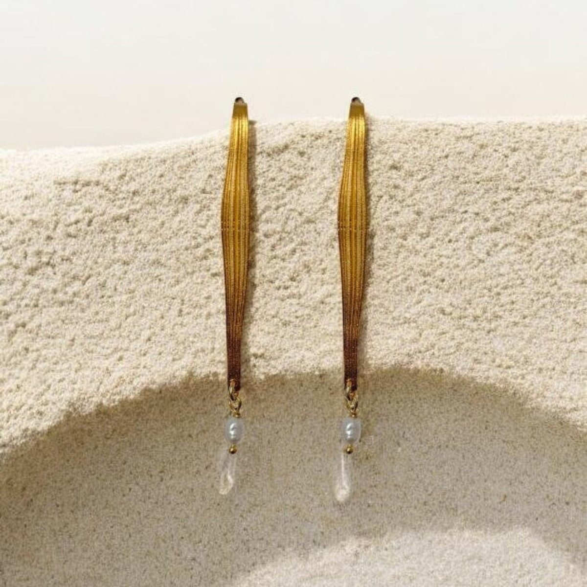 Gold hoop earrings with pearl-like beads hanging on a textured beige surface.
