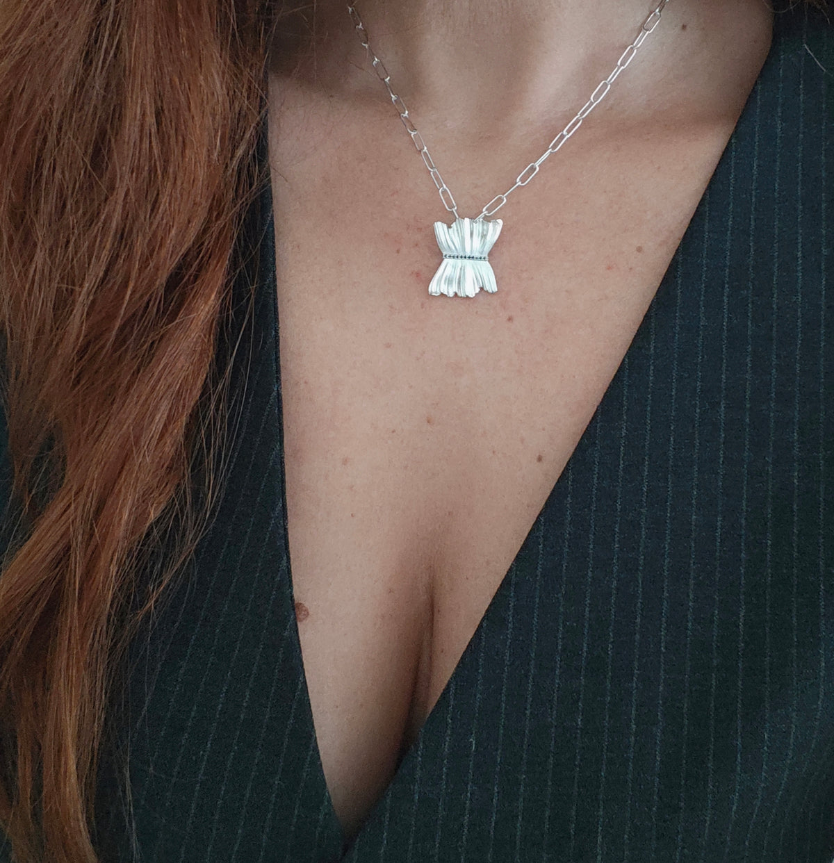 Silver necklace with a unique pendant worn by a person in a black outfit.