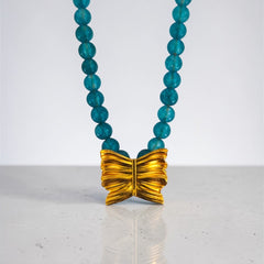 Necklace with blue beads and a gold bow pendant on a white background