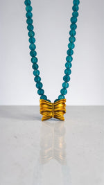 Necklace with blue beads and a gold bow pendant on a white background