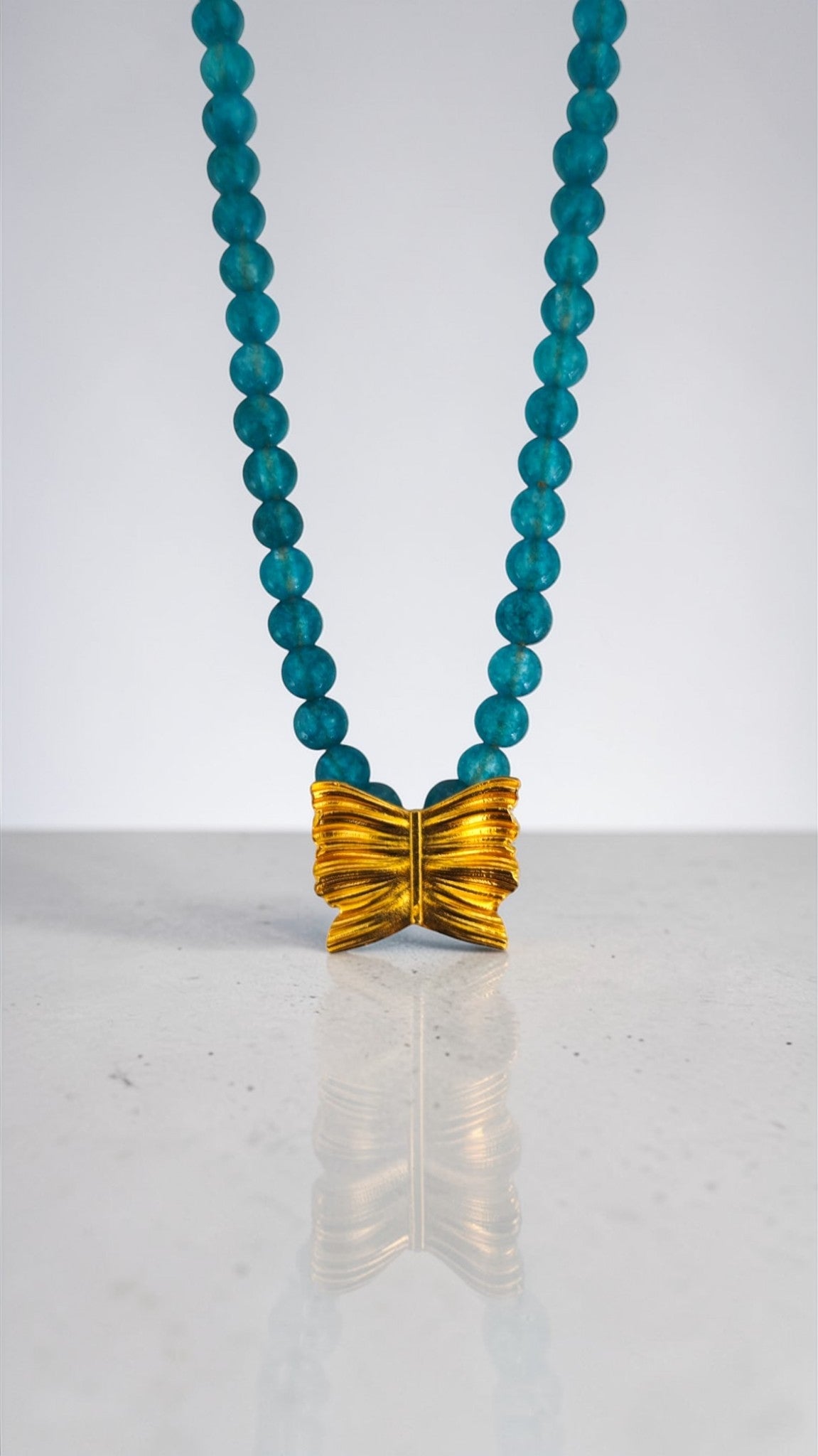 Necklace with blue beads and a gold bow pendant on a white background