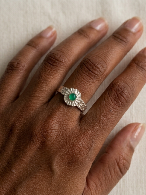 Silver ring with a green gemstone on a hand against a neutral background