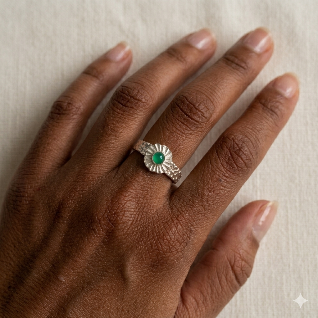 Silver ring with a green gemstone on a hand against a neutral background