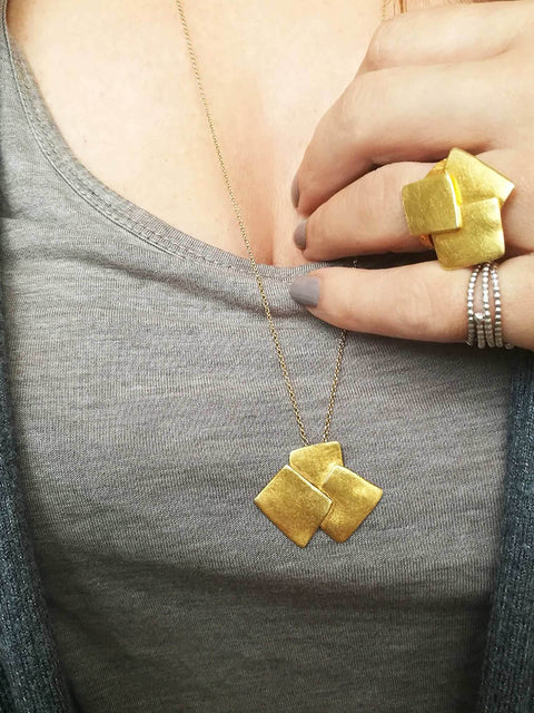 Hand wearing Athenart Bouquet Ring and matching pendant – golden sculptural jewelry.