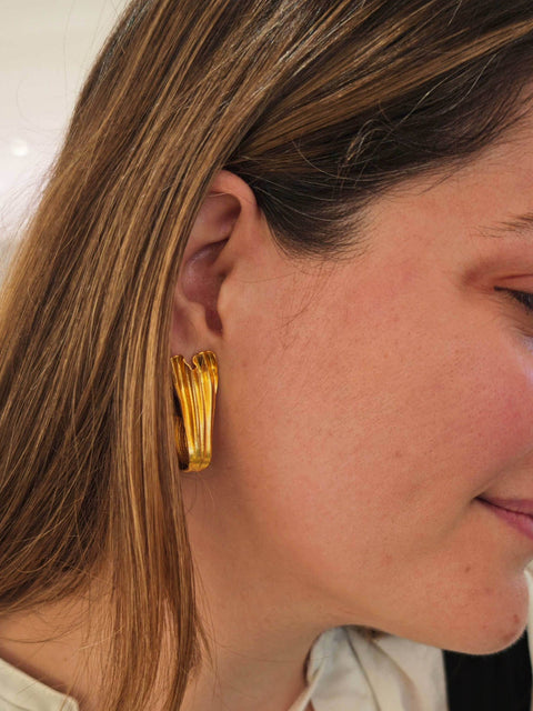 Model smiling while wearing Swan Hoops – graceful gold statement earrings.
