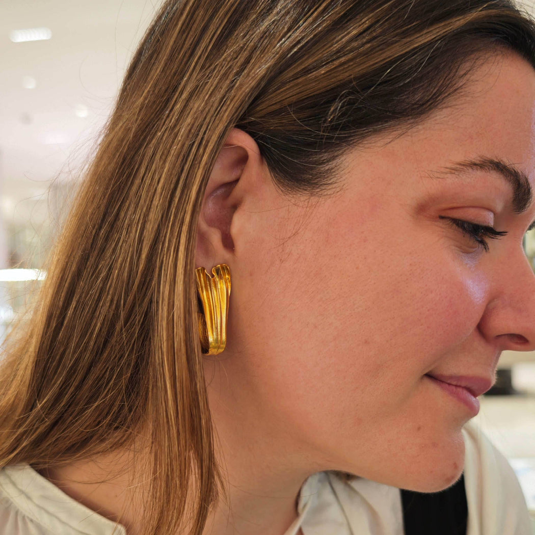 Model smiling while wearing Swan Hoops – graceful gold statement earrings.