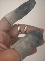 A close-up of a hand wearing two slim gold rings, with gray fabric finger sleeves covering the fingers against a plain light background.
