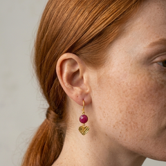 Close-up of a person wearing gold love ( heart ) earrings with a ruby  stone by Athenart made in Athens 