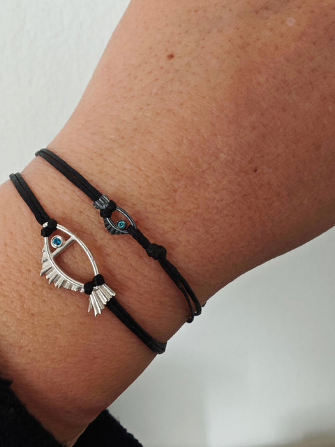 Black bracelet with a silver eye-shaped Fish charm on a wrist against a white background
