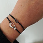 Black bracelet with a silver eye-shaped Fish charm on a wrist against a white background
