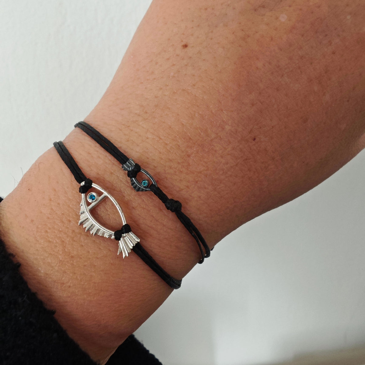 Black bracelet with a silver eye-shaped Fish charm on a wrist against a white background