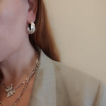 Model wearing Athenais Drapé Hoops in polished silver with layered chain and Peplos pendant, lifestyle portrait
