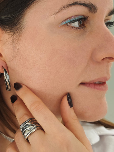 Close-up of a woman adjusting an earring with a neutral background