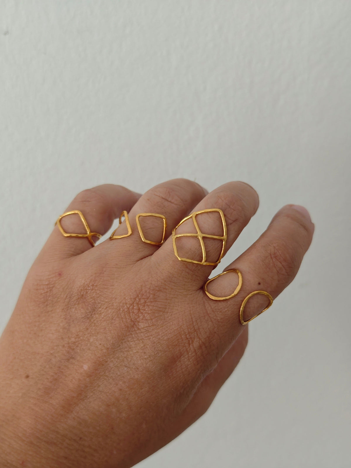 Hand wearing gold geometric ring on a plain background