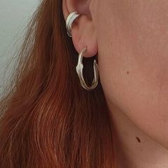 Woman wearing Twirl Peplos hoop earrings, twisted textured sterling silver hoops