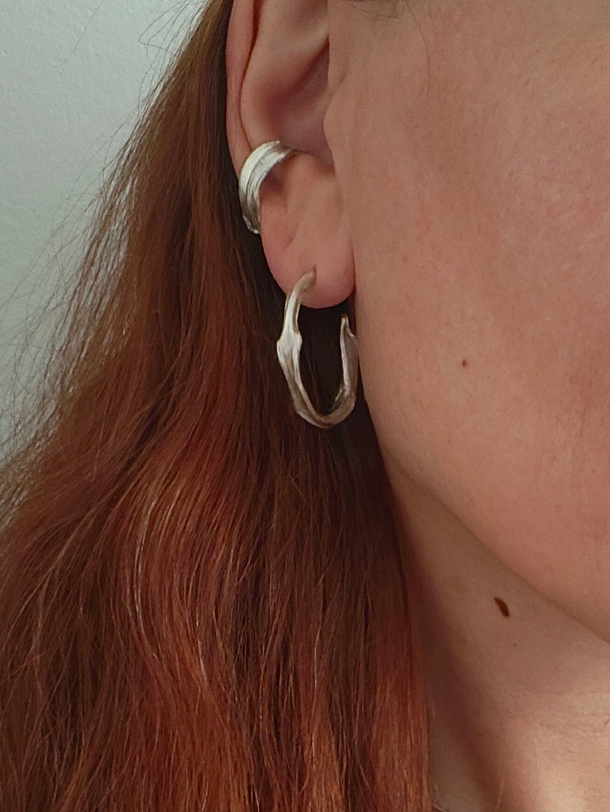 Woman wearing Twirl Peplos hoop earrings, twisted textured sterling silver hoops