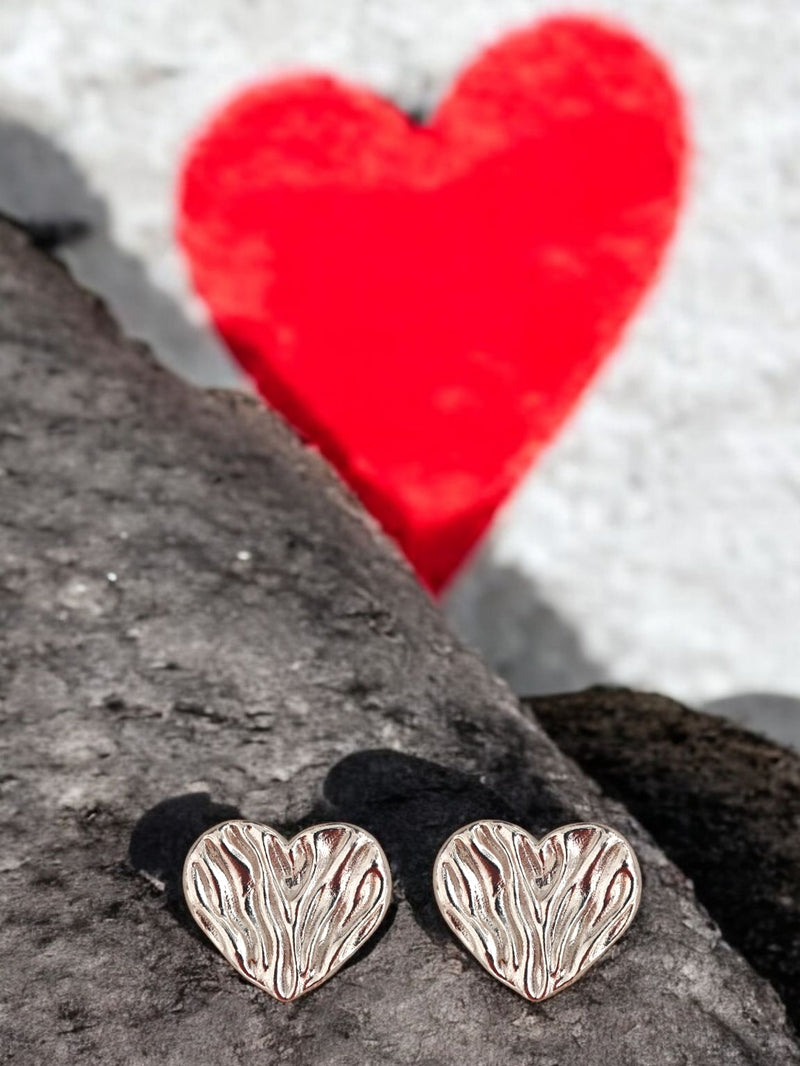 Heart-shaped silver earrings on a rock with a red heart in the background