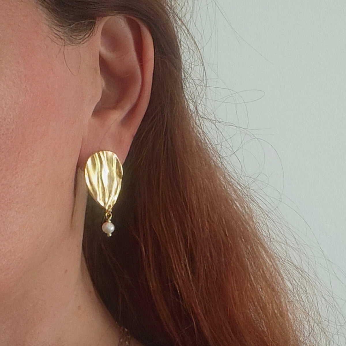 Woman wearing Peplos pearl drop earring, gold teardrop with pearl detail