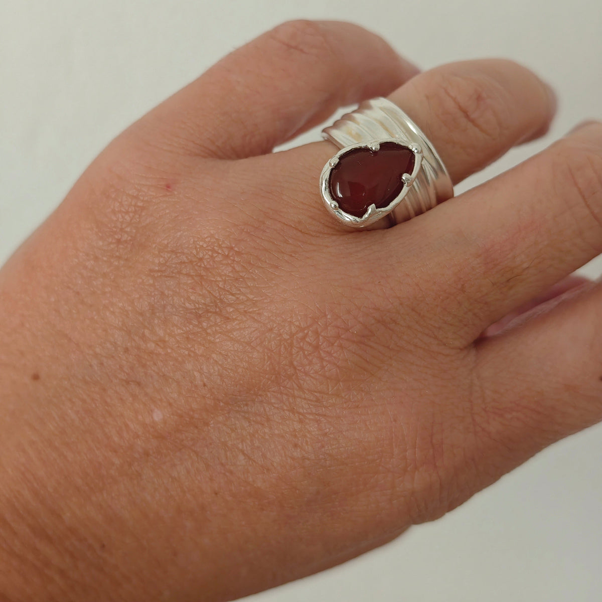 Naiás carnelian ring in sterling silver on hand, wide draped adjustable bandbackground