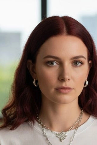 Close-up of Athenais Drapé Hoop in silver on ear, paired with chain necklace and Peplos pendant, warm light