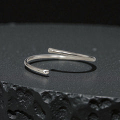 Minimal sterling silver open bangle cuff bracelet on black textured surface