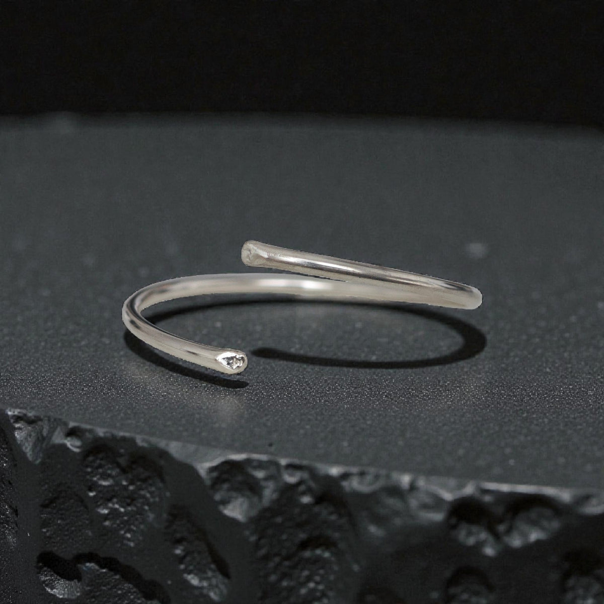 Minimal sterling silver open bangle cuff bracelet on black textured surface