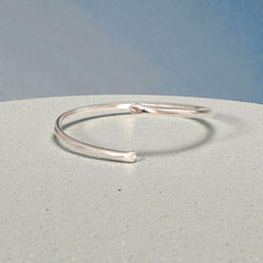 Polished sterling silver open bangle bracelet on light stone surface