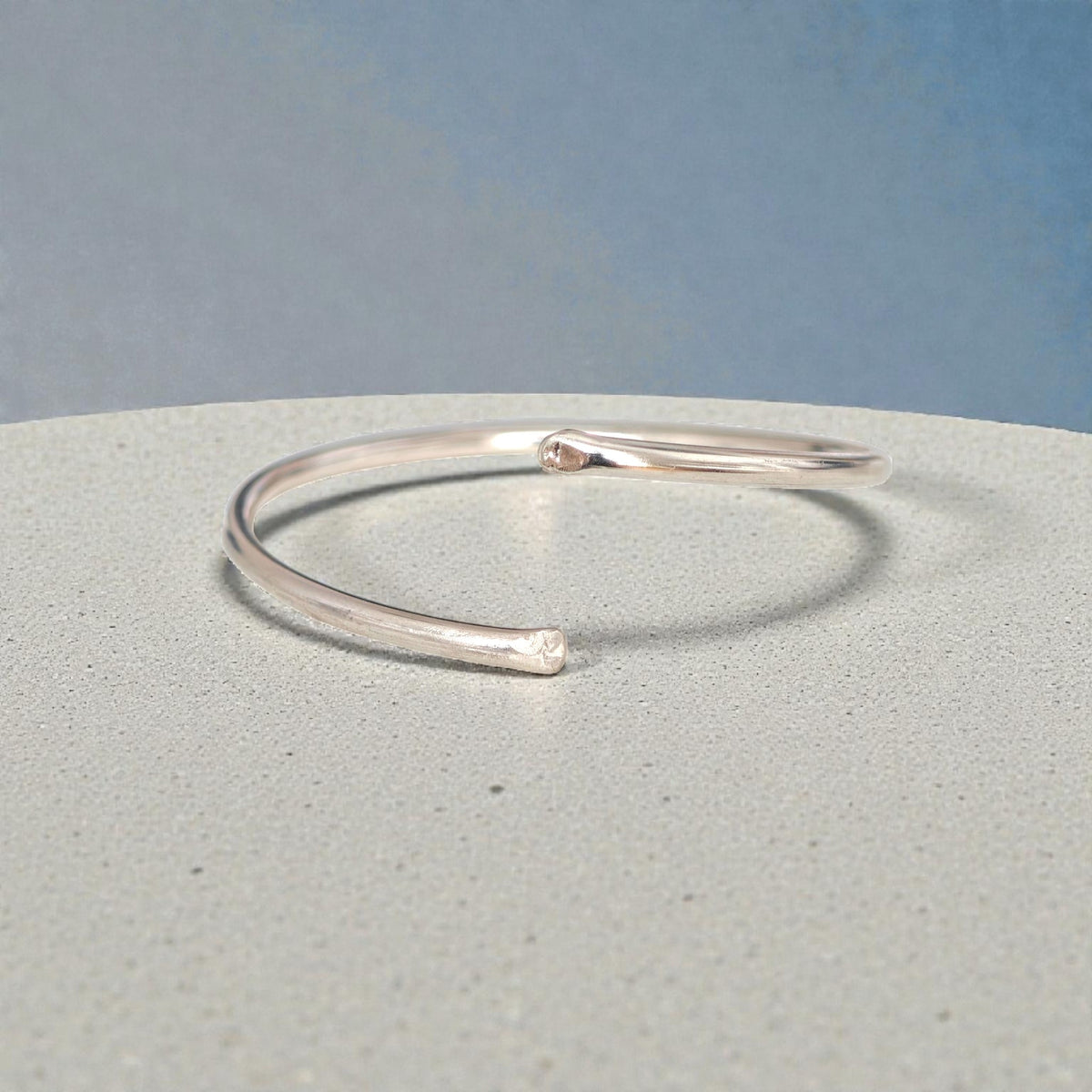 Polished sterling silver open bangle bracelet on light stone surface