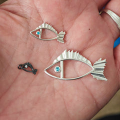 Three silver fish-shaped pendants on a person's palm.