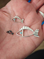 Three silver fish-shaped pendants on a person's palm.