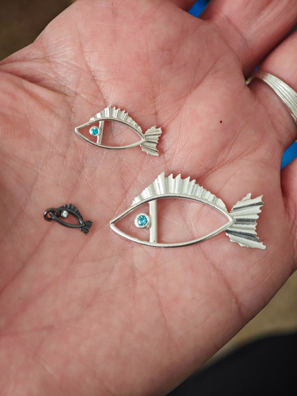 Three silver fish-shaped pendants on a person's palm.