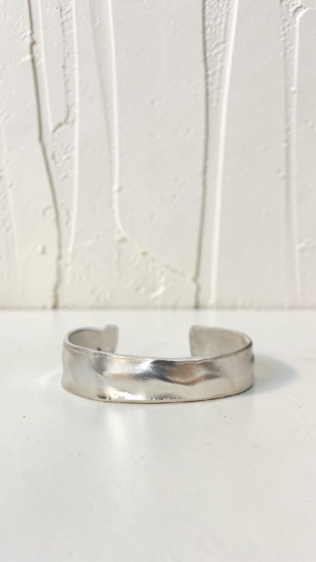 Silver bracelet on a white surface with a light gray background