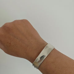 Silver bracelet on a wrist against a plain background