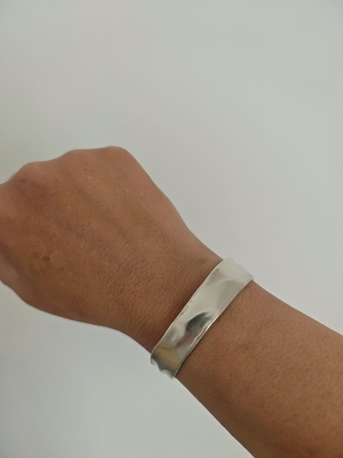 Silver bracelet on a wrist against a plain background