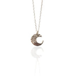 A silver crescent moon pendant necklace with a textured, hammered finish, hanging from a delicate silver chain against a white background with a soft reflection below.