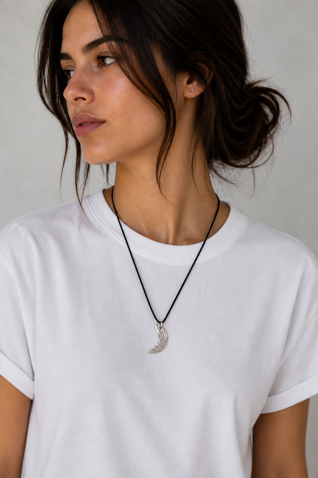 Woman wearing a white t-shirt and a necklace with a pendant against a neutral background