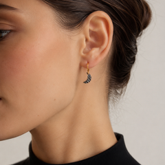 Brunette model wearing a small crescent moon earring with a gold hoop and dark textured charm, shown in a close-up side profile against a soft neutral background.