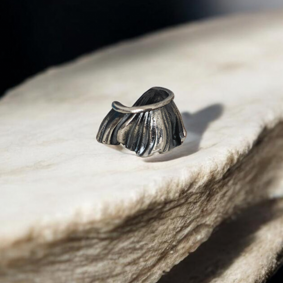 Sculptural oxidized silver ear cuff inspired by shell forms on natural stone