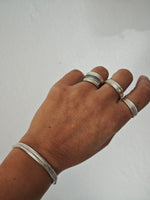 Hand wearing multiple silver rings on a plain background