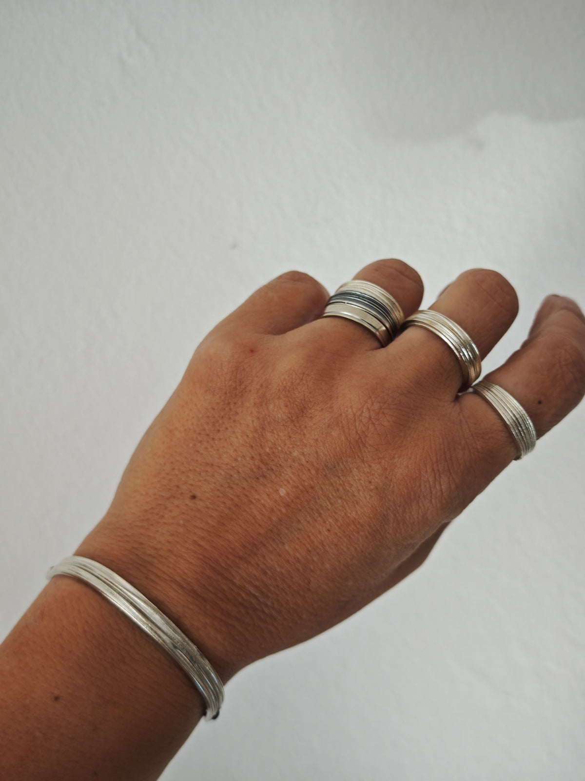Hand wearing multiple silver rings on a plain background